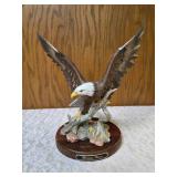 Homco "Majestic Wings" bald10" eagle figurine. It is a porcelain sculpture depicting a bald eagle landing on a rocky mound and is mounted on a dark wooden base with a plaque reading "Majestic Wings". 