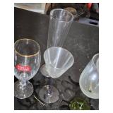 Mixed glassware including Stella Artois glasses, wine glasses with green stems, and a decorative bottle with a crown top.
