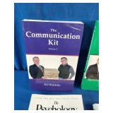 Collection of six self-improvement, financial literacy, leadership, and communication books laid out on a blue fabric surface.