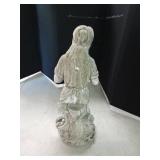 Cement statue of a lady sitting on a tree stump holding a water pitcher with a basket of fruit alongside her