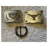 Western-themed belt buckles including intricate wagon design, longhorn motif, and a rhinestone-studded buckle