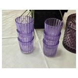 Artificial lavender plant in a black pot, set of purple glasses, and a purple glass container with lid