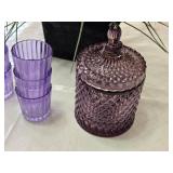 Artificial lavender plant in a black pot, set of purple glasses, and a purple glass container with lid