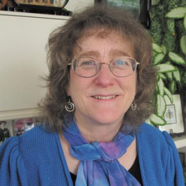 Eleanor Levin wearing blue shirt and blue/purple scarf, blonde hair, wire framed glasses