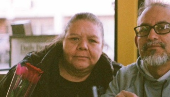 A middle-aged couple sitting close together at a table with a small bouquet of roses in front of them.