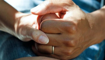 Close-up of two people holding hands in a comforting and supportive gesture, one wearing a gold ring.