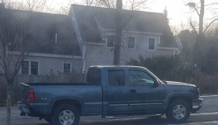 A blue Chevrolet Z71 pickup truck parked on a residential street in front of a two-story house.