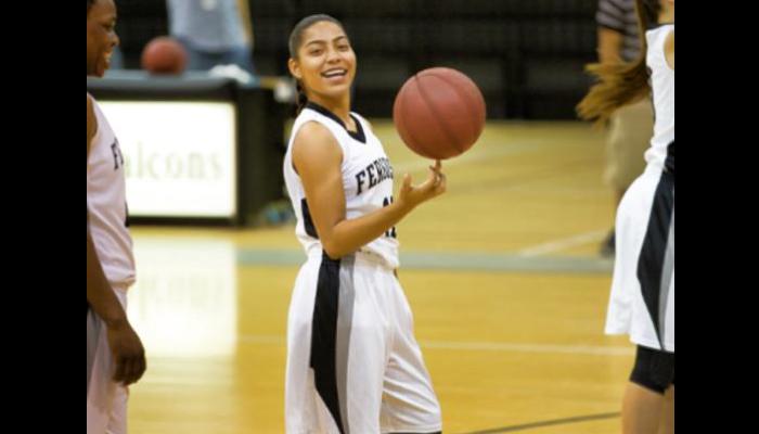 A young female basketball player in a white jersey smiles as she spins a basketball on her fingertip.