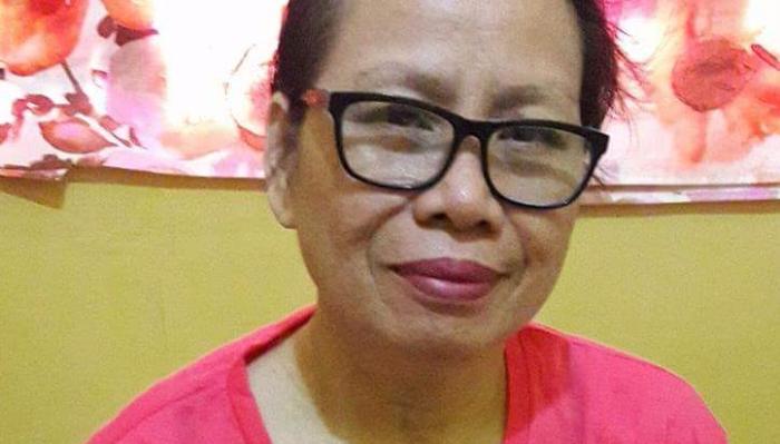 A smiling woman with short hair, black-rimmed glasses, and a bright pink shirt.
