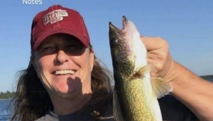 A smiling person wearing a red cap holding up a freshly caught fish on a sunny day.