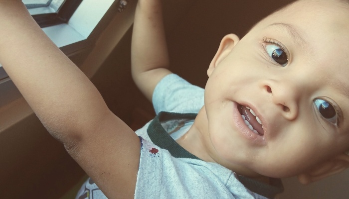 A young toddler with big dark eyes smiling playfully with arms raised.