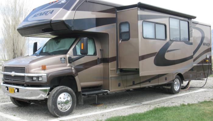 Large brown and tan Seneca motorhome RV parked at a campsite with slide-outs extended.