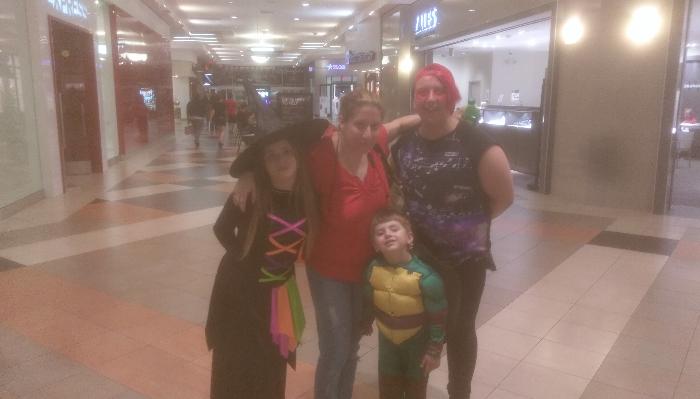 A family posing in a shopping mall dressed in Halloween costumes, including a witch and a Ninja Turtle.