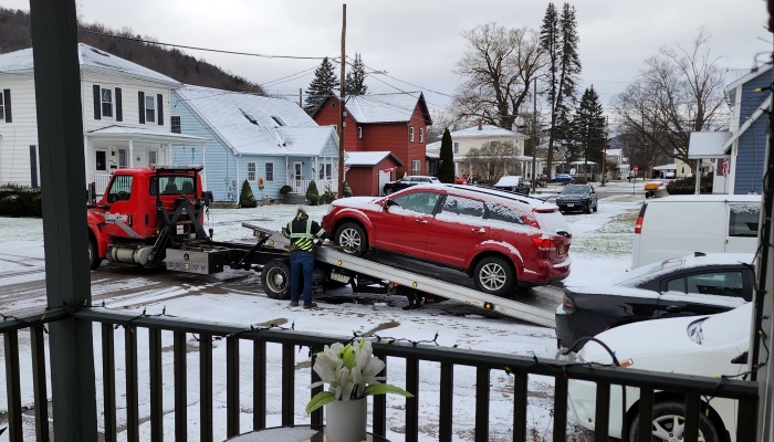 A tow truck driver loads a red SUV onto a flatbed tow truck on a snowy residential street.