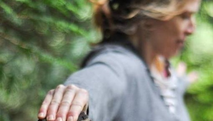Woman in a grey sweater practicing yoga outdoors surrounded by lush green foliage.