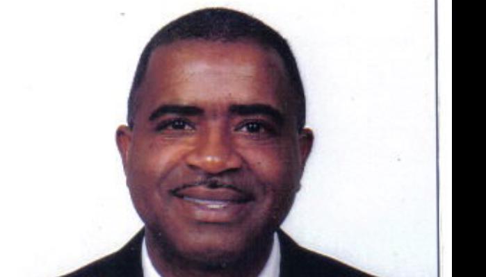 Headshot of a smiling Black man with short hair and a thin mustache wearing a dark suit jacket.