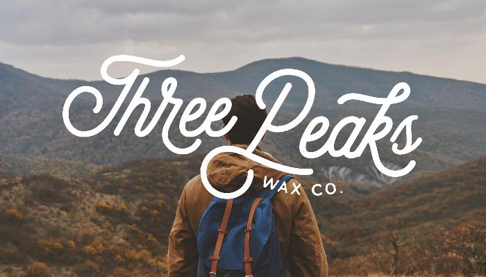 A hiker with a blue backpack looks out at mountain peaks, overlaid with text reading "Three Peaks Wax Co."