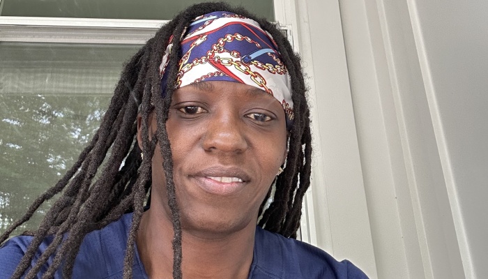 Close-up of a person with long dark locs wearing a patterned headband, smiling gently at the camera.