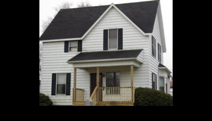 A two-story white house with black shutters, a dark roof, and a wooden front porch.