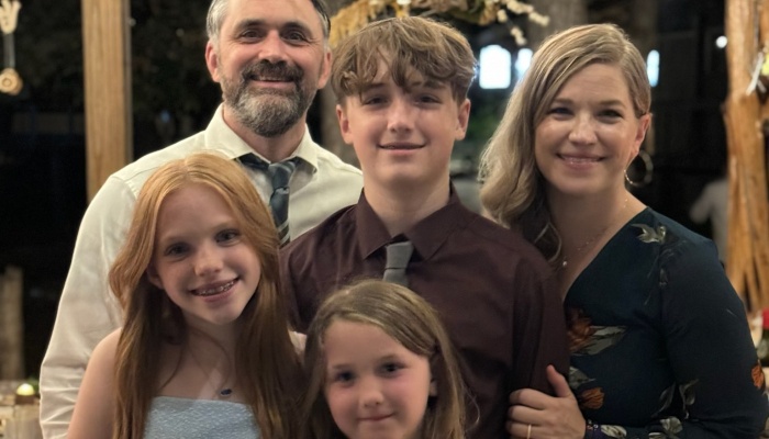 A smiling family of five, including parents and three children, posing together in formal attire.
