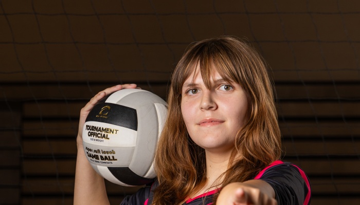Young female athlete holding a volleyball next to her face and pointing directly towards the camera.