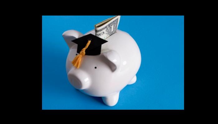 White piggy bank wearing a mini graduation cap with a dollar bill in its coin slot against a blue background.