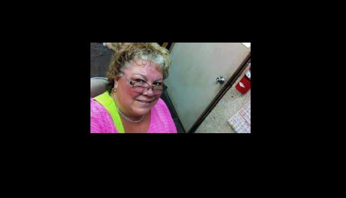 A smiling woman with curly hair and glasses wearing a bright pink top.
