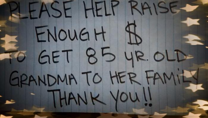 Handwritten sign reading: "PLEASE HELP RAISE ENOUGH $ TO GET 85 YR. OLD GRANDMA TO HER FAMILY THANK YOU!!"