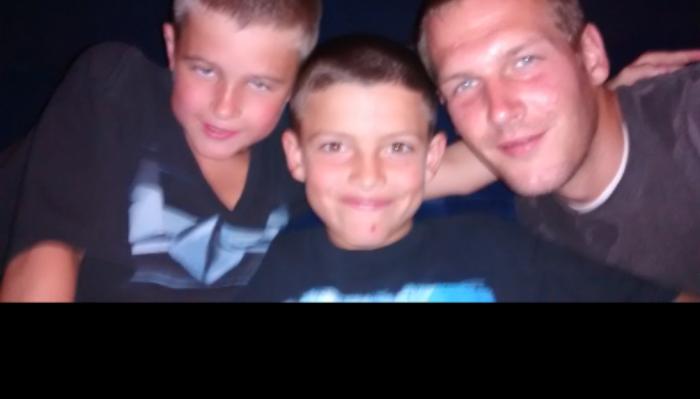 A smiling man and two young boys posing closely together.
