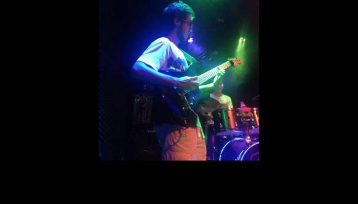 A guitarist playing electric guitar live on stage under blue and green concert lights.