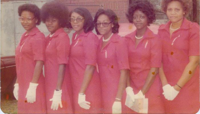 Six Black women standing together in matching red vintage dresses and white gloves.
