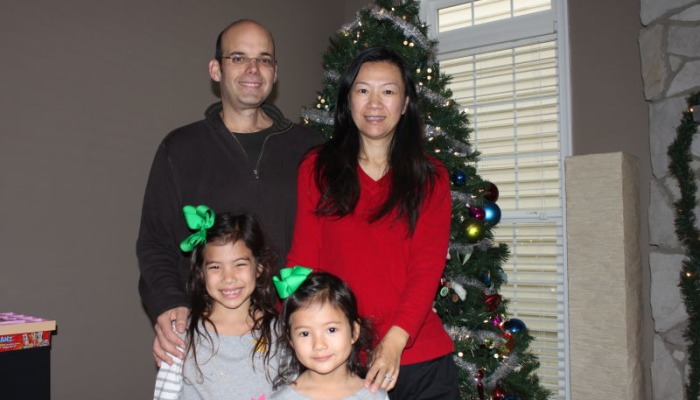 A smiling family of four standing together in front of a decorated Christmas tree.