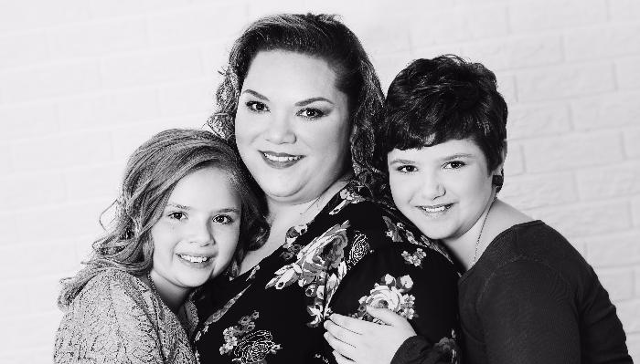 Black and white portrait of a smiling mother posed closely with her two children.