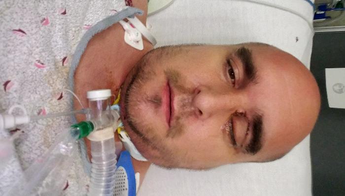 A man in a hospital bed with a tracheostomy tube connected to his neck.