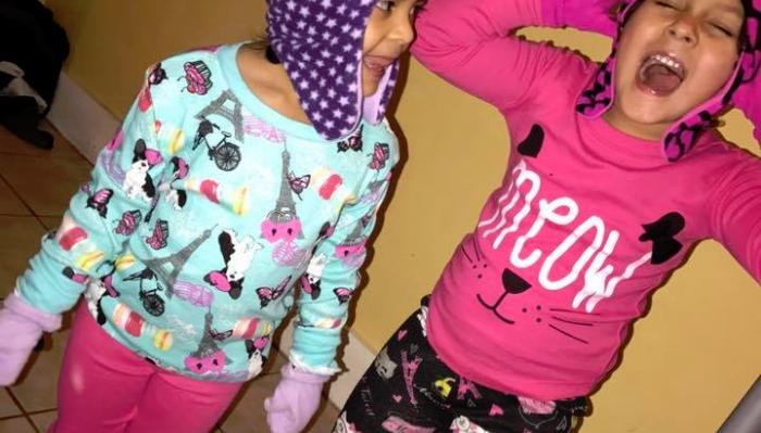 Two young girls wearing colorful winter hats and warm long-sleeve shirts laughing joyfully together.