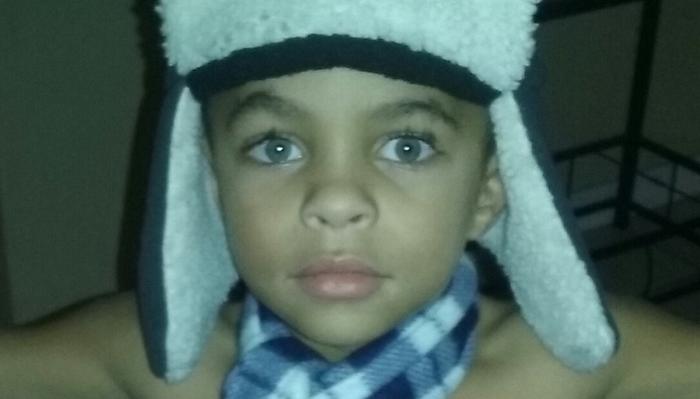 Close-up of a young boy with light blue eyes wearing a plush winter trapper hat and plaid scarf.