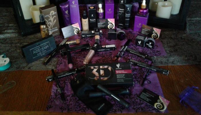 A collection of Younique cosmetics, skincare products, and brushes displayed on a patterned purple cloth.