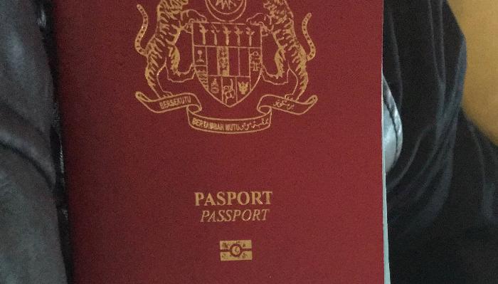 Red Malaysian passport cover featuring a gold coat of arms emblem and the words PASPORT PASSPORT.