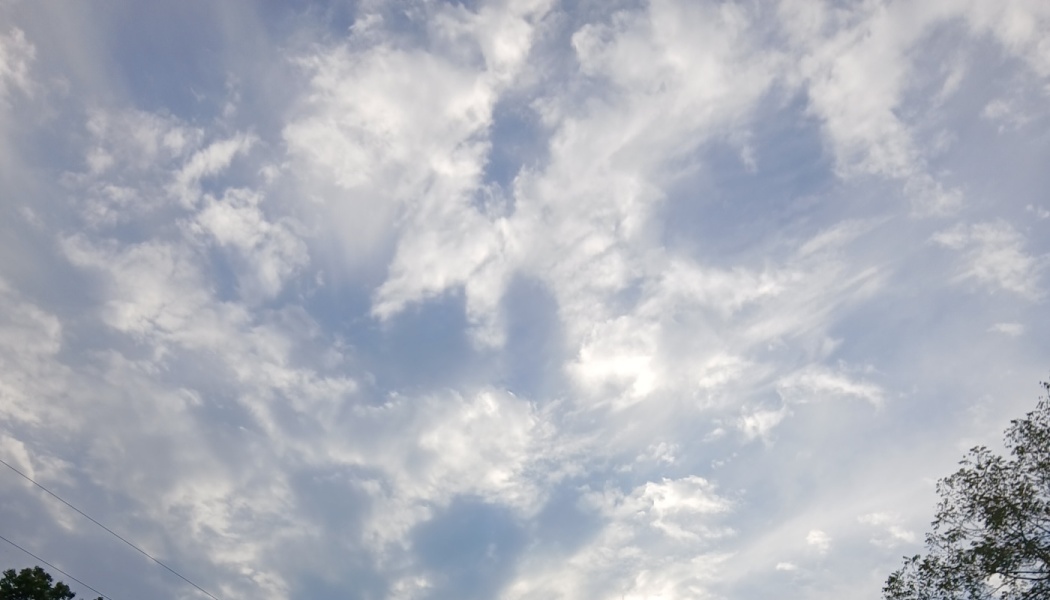 Wispy white clouds scattered across a light blue sky with sunlight peeking through.