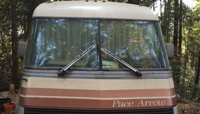 Front view of a vintage beige Pace Arrow motorhome parked in a forest.
