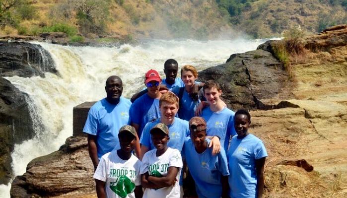 Diverse group of young volunteers posing together in front of a large, powerful waterfall.