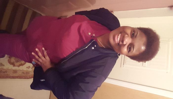 A smiling woman wearing maroon medical scrubs and a dark jacket posing with her hand on her hip.
