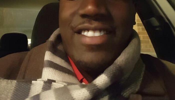 Close-up of a smiling man wearing a striped scarf and dark coat inside a car.