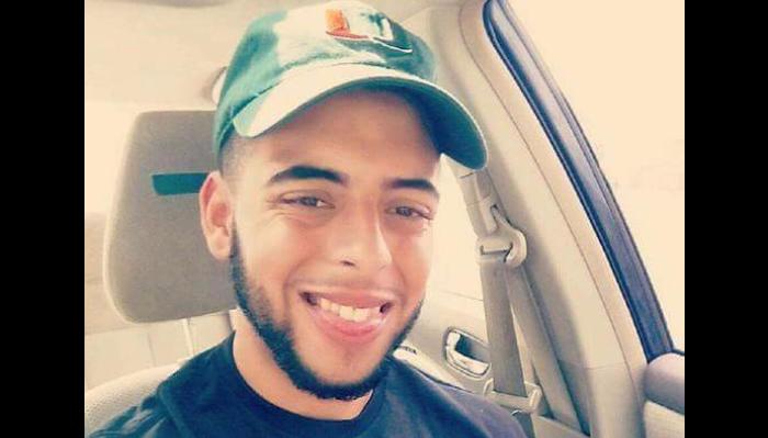 A young man with a beard wearing a green baseball cap smiling inside a car.