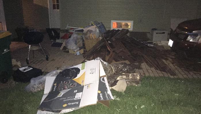 Piles of wooden debris, cardboard boxes, and damaged household items outside a house at night.