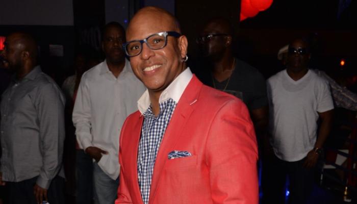 A smiling bald man wearing blue glasses and a bright red blazer at an event.