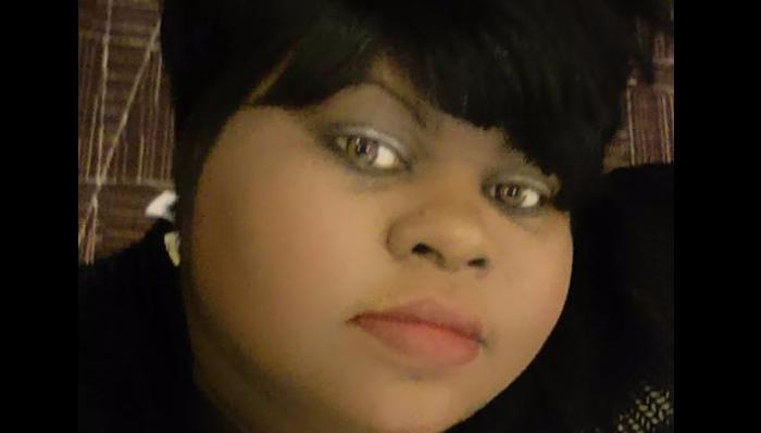 Close-up portrait of a Black woman with short dark hair, bangs, and hazel eyes looking at the camera.