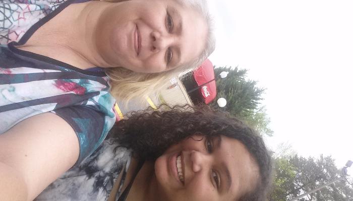 A blonde woman and a younger woman with dark curly hair smiling together for an outdoor selfie.