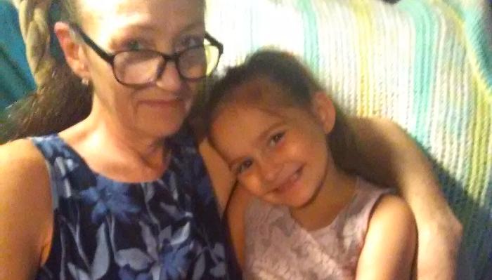 A smiling woman with glasses embracing a young girl who leans affectionately against her.