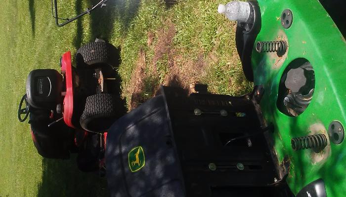 A red Husqvarna riding mower parked next to a green John Deere lawn tractor on grass.